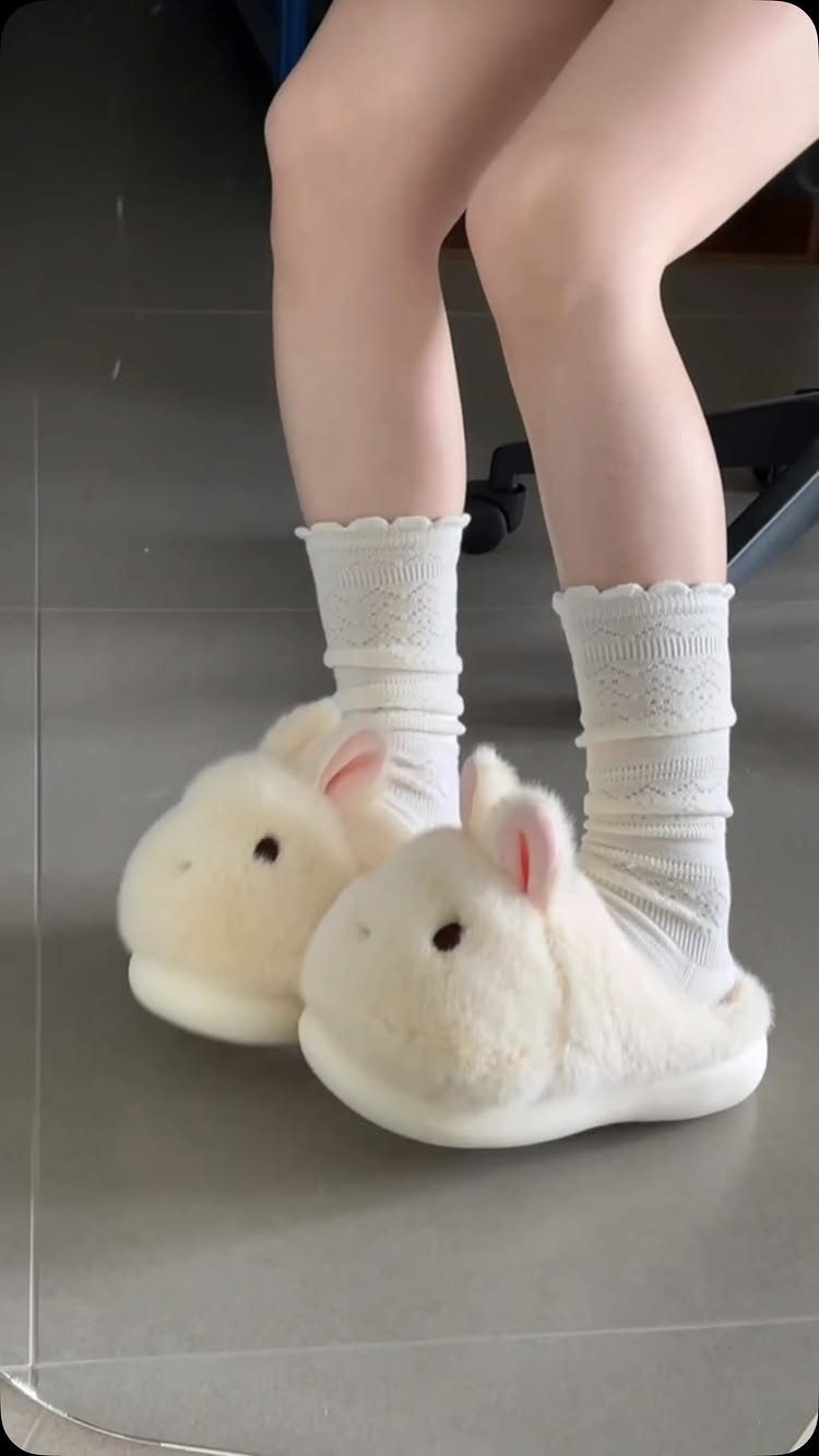Cream-colored plush bunny slippers worn with white lace socks on a grey floor.