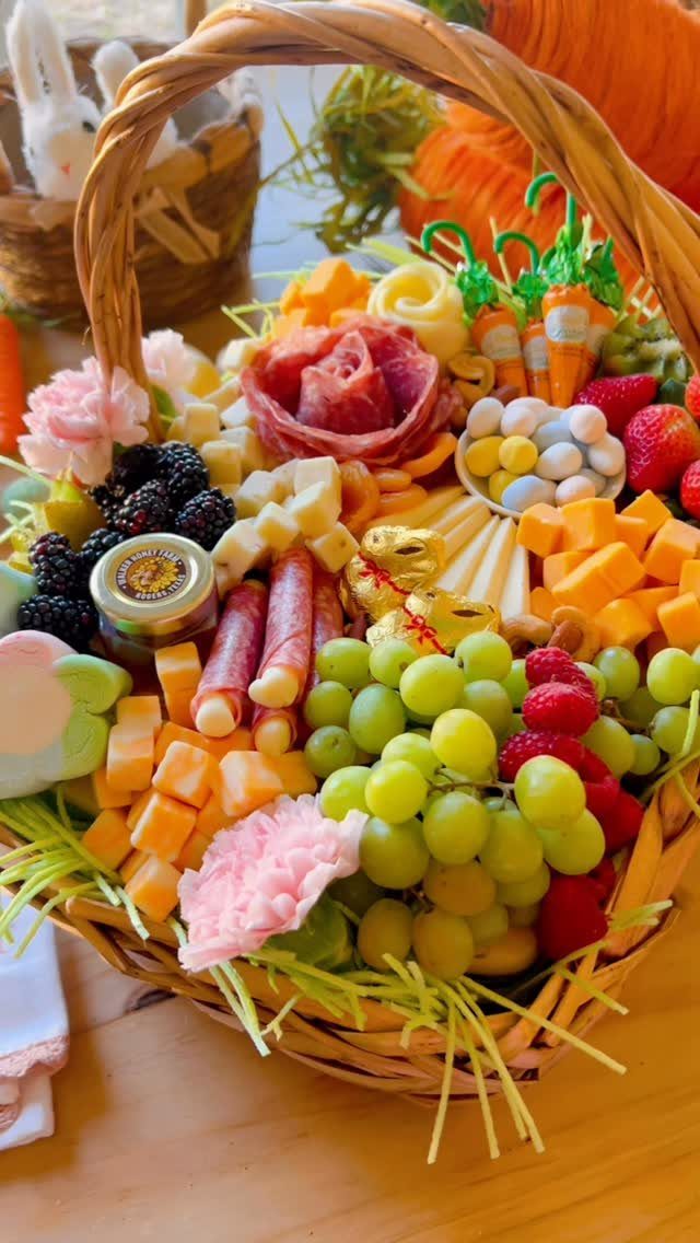 Wicker basket filled with charcuterie, fresh fruits, cheeses, and pink floral accents.