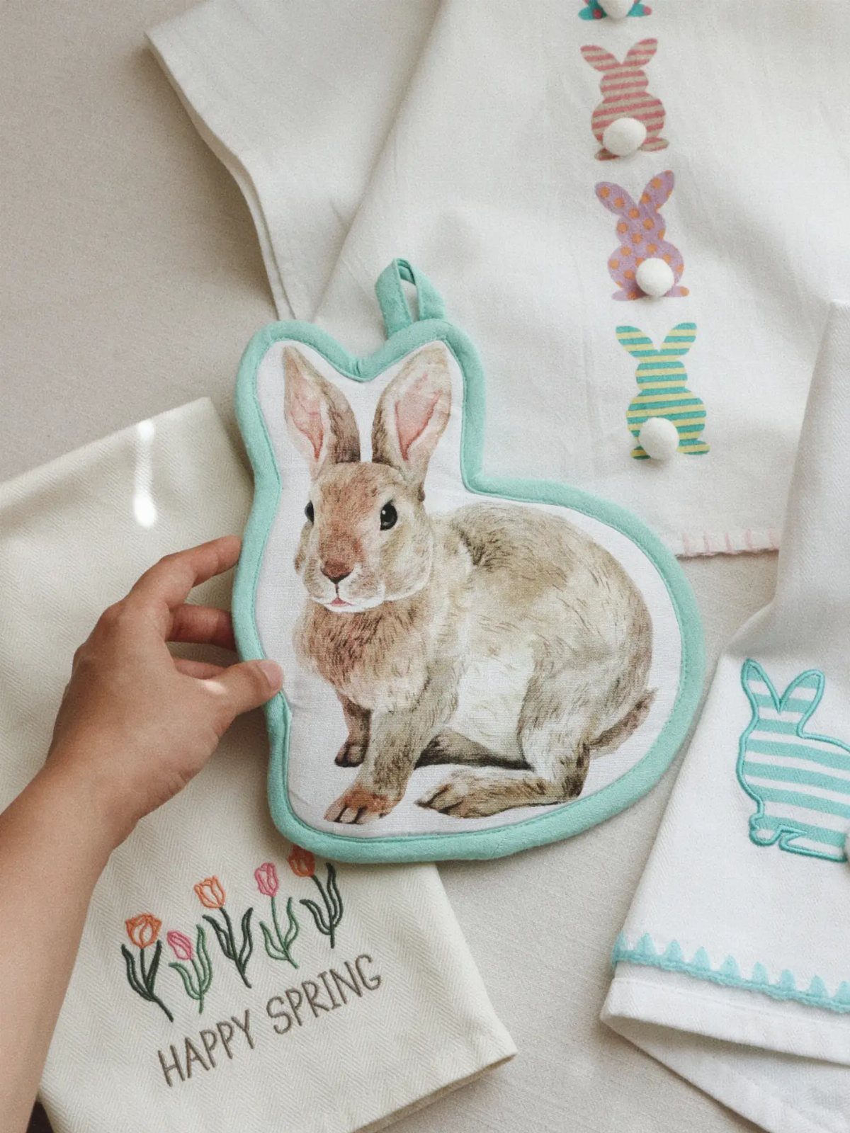 Bunny-shaped pot holder and white towels with spring embroidery and rabbit illustrations.