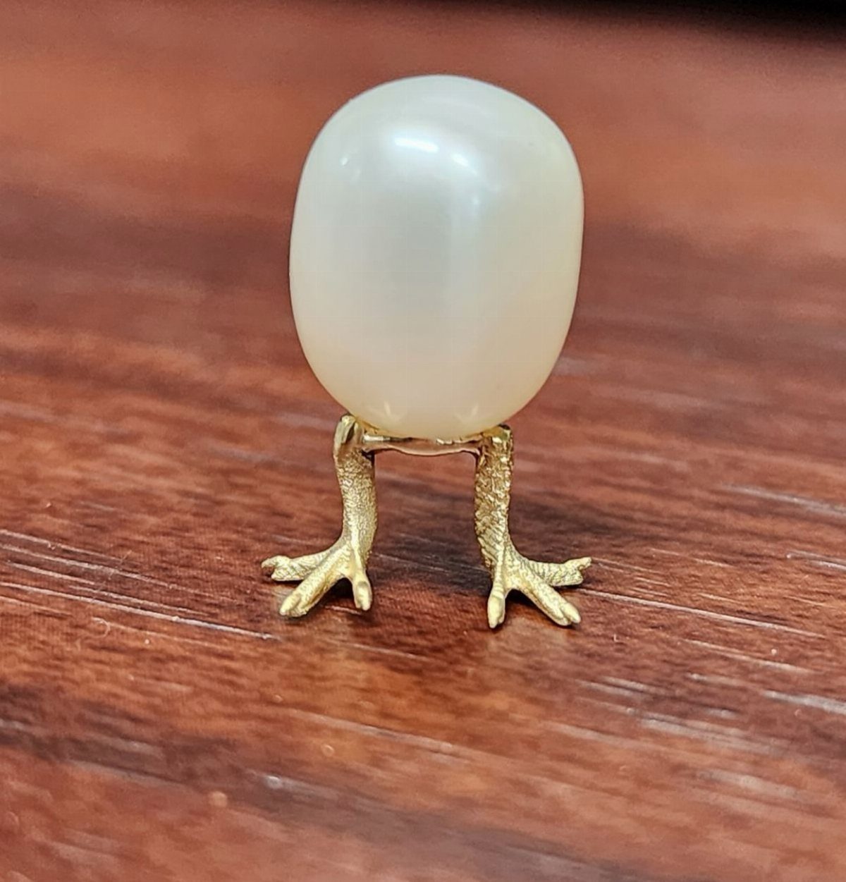White egg jewelry with gold bird legs on a brown wooden surface