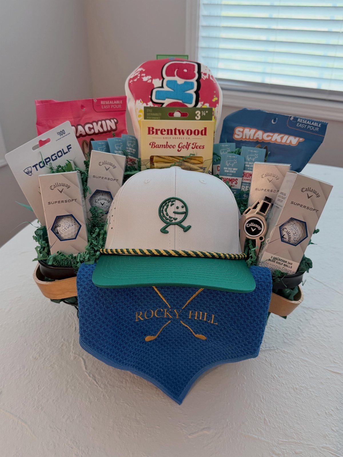 Golf gift basket containing a white cap, blue towel, tees, and golf balls.