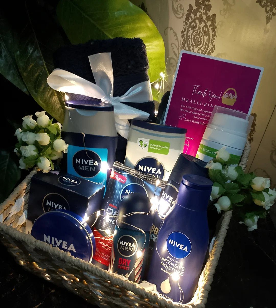 Wicker gift basket with Nivea Men skincare products, a blue towel, and fairy lights.