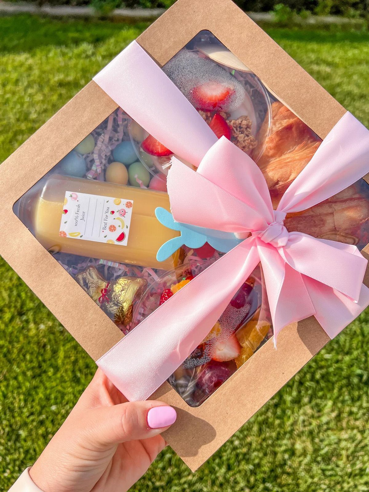 Easter gift box with pastries, strawberries, and colorful eggs tied with pink ribbon