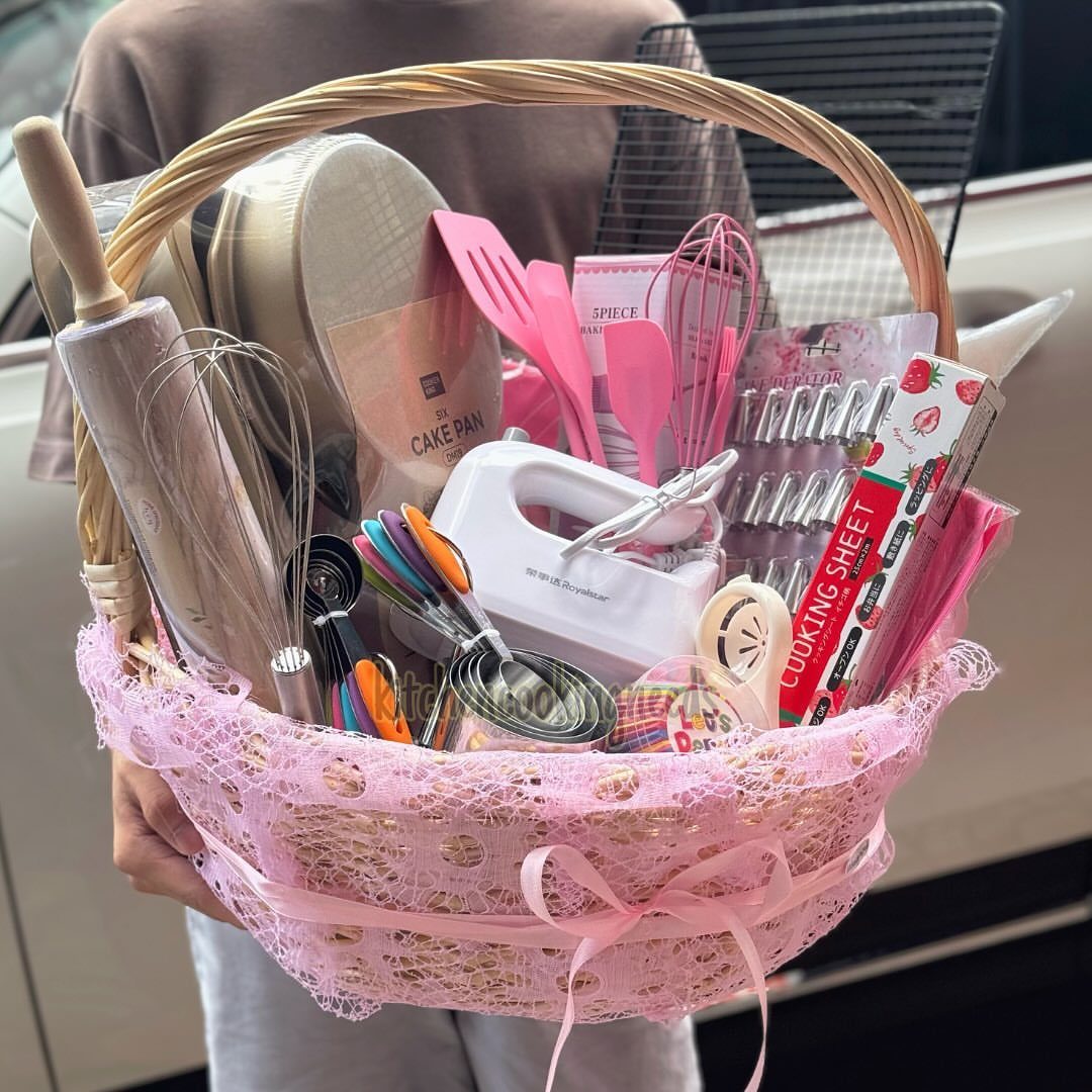 Baking kit basket with pink lace, containing a hand mixer, whisks, and spatulas.