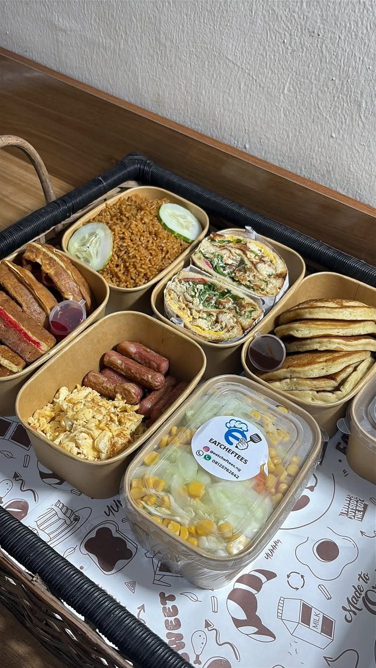 Breakfast basket with eggs, sausages, pancakes, wraps, and fried rice in cardboard containers.