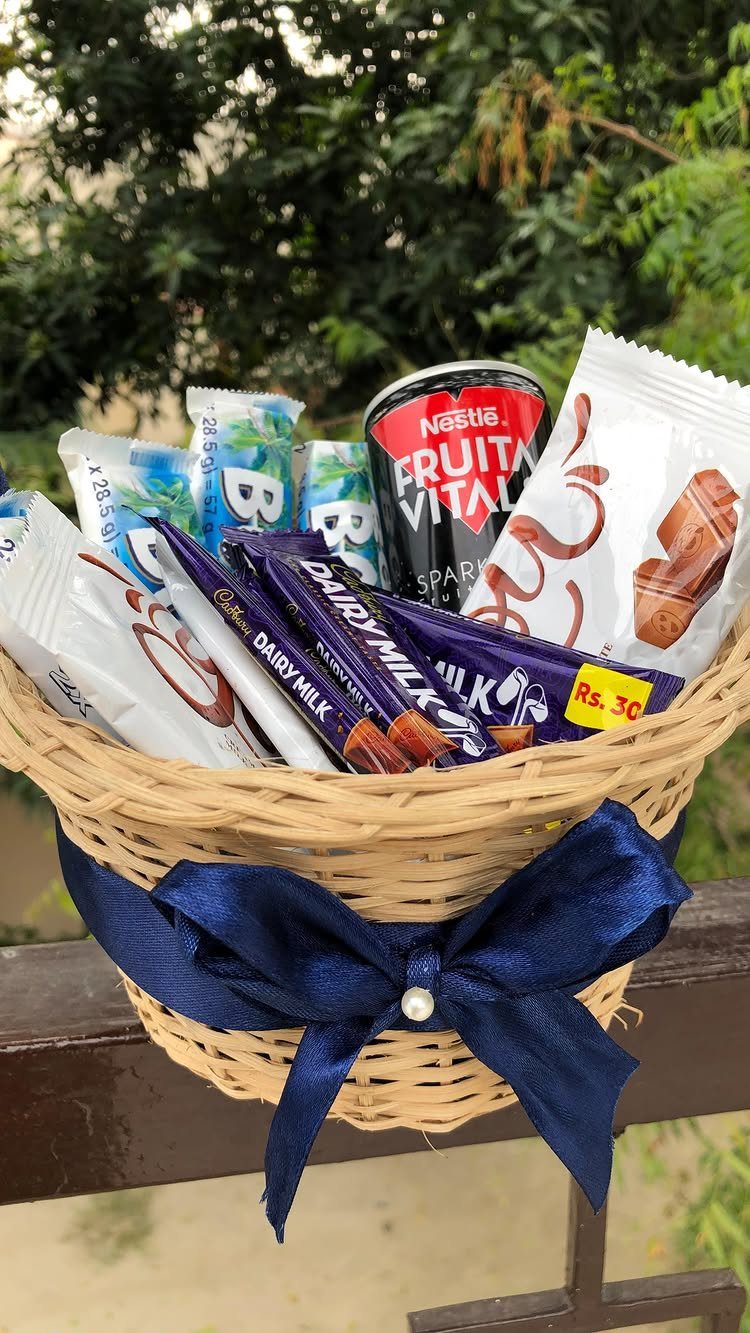 Wicker gift basket filled with chocolate bars and a drink with blue bow.