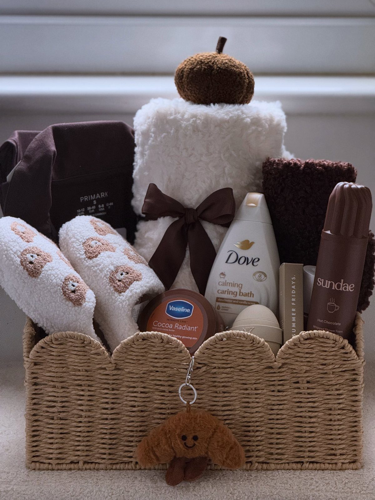 Woven gift basket containing fuzzy socks, a plush blanket, Dove soap, and chocolate.
