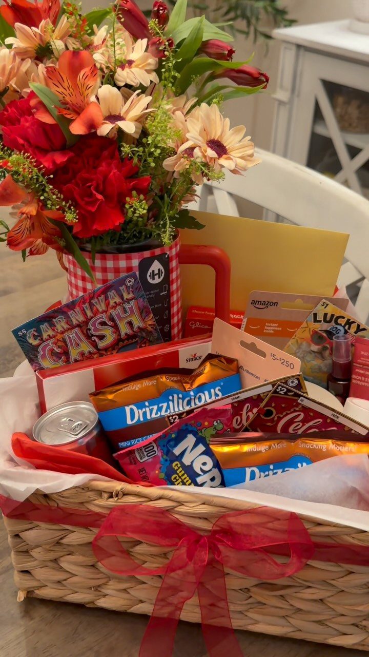 Woven gift basket with red ribbon, colorful candies, and a floral bouquet mug.