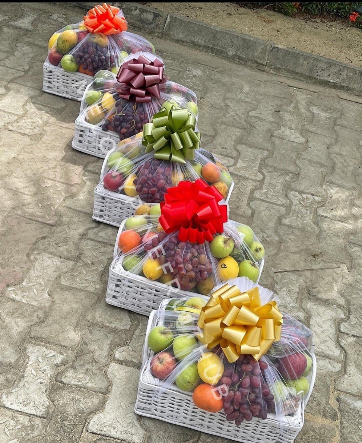 Five white wicker fruit baskets wrapped in cellophane with colorful decorative bows.