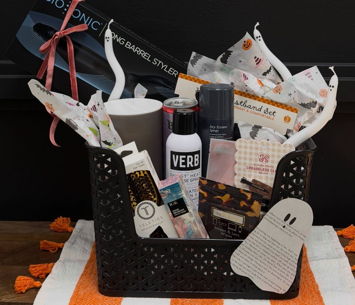 Black gift basket filled with beauty products and ghost decorations on striped cloth.