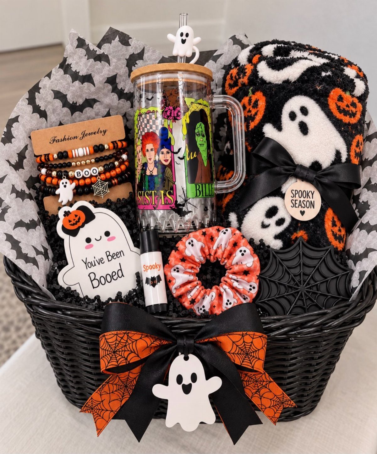 Halloween gift basket with ghost blanket, themed tumbler, jewelry, and spooky accessories.