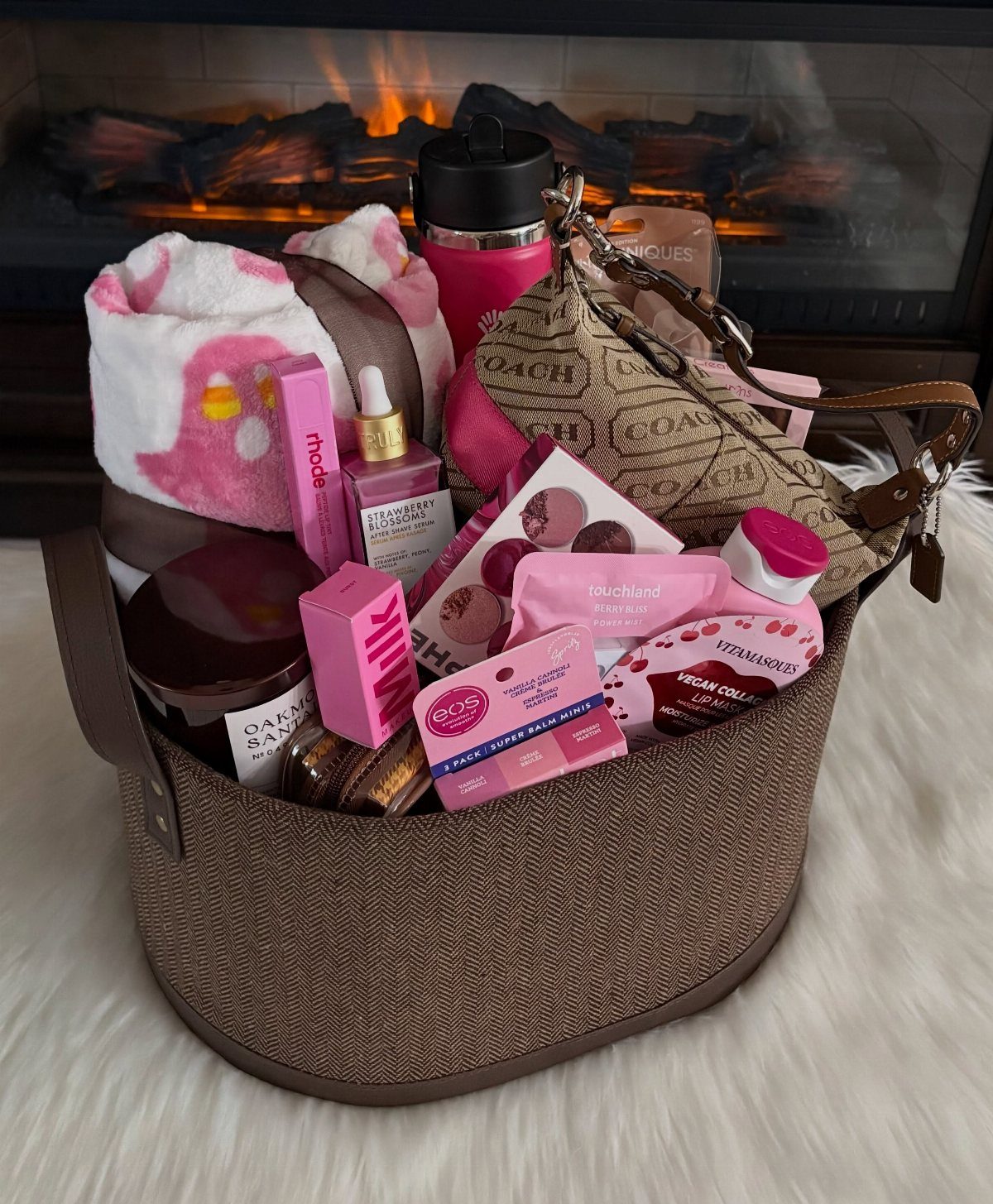 Brown woven tote bag filled with pink beauty products and cozy accessories.