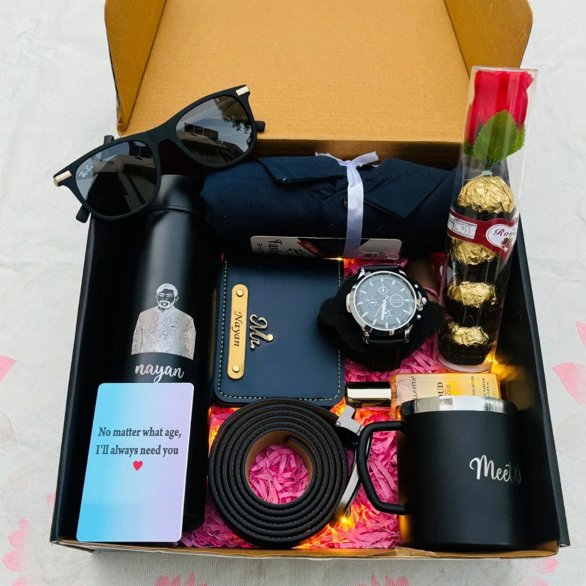 Gift box with black accessories, a blue shirt, and chocolates on pink filler.