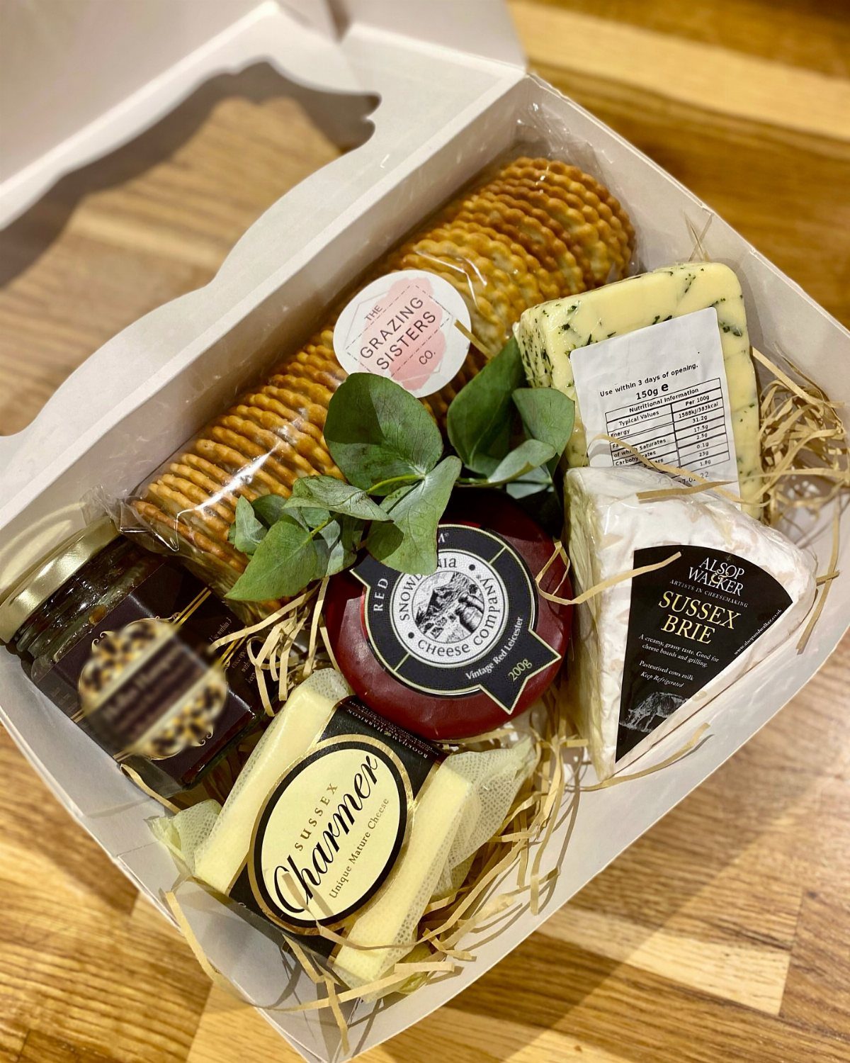 Cheese gift basket with brie, crackers, and chutney in a white box.