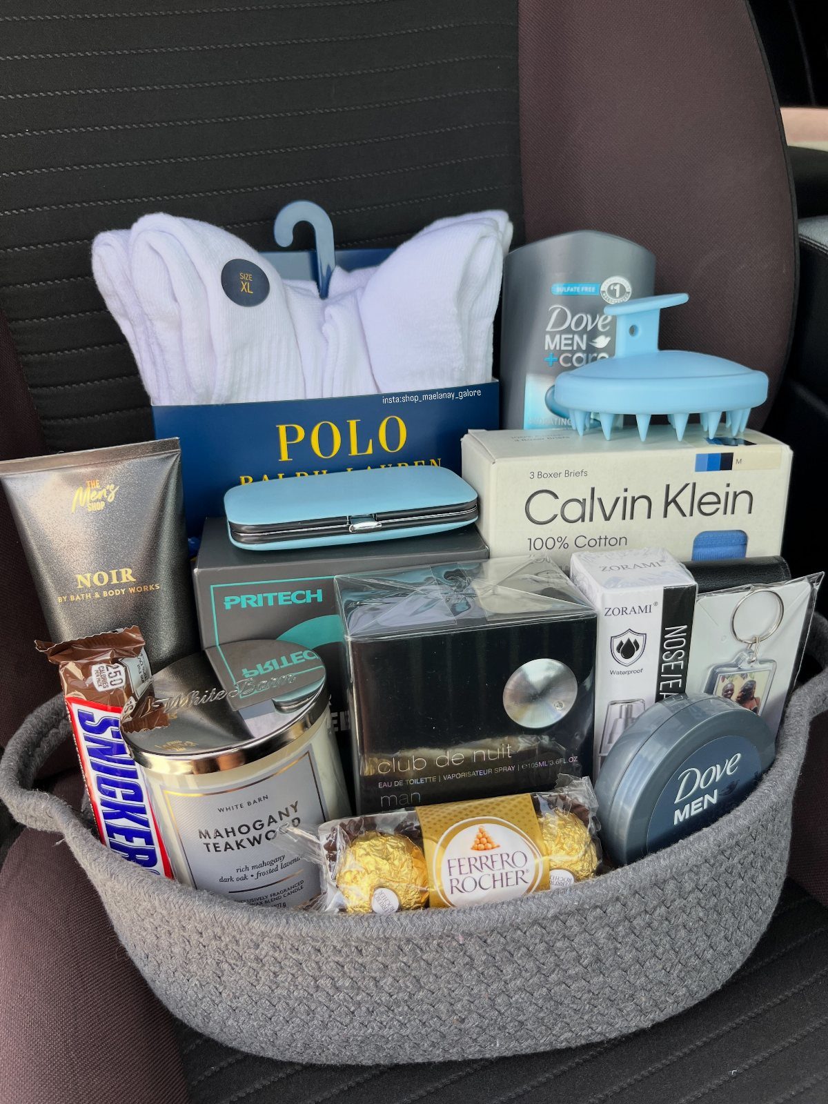 Grey gift basket filled with men's grooming products, towels, and chocolates.