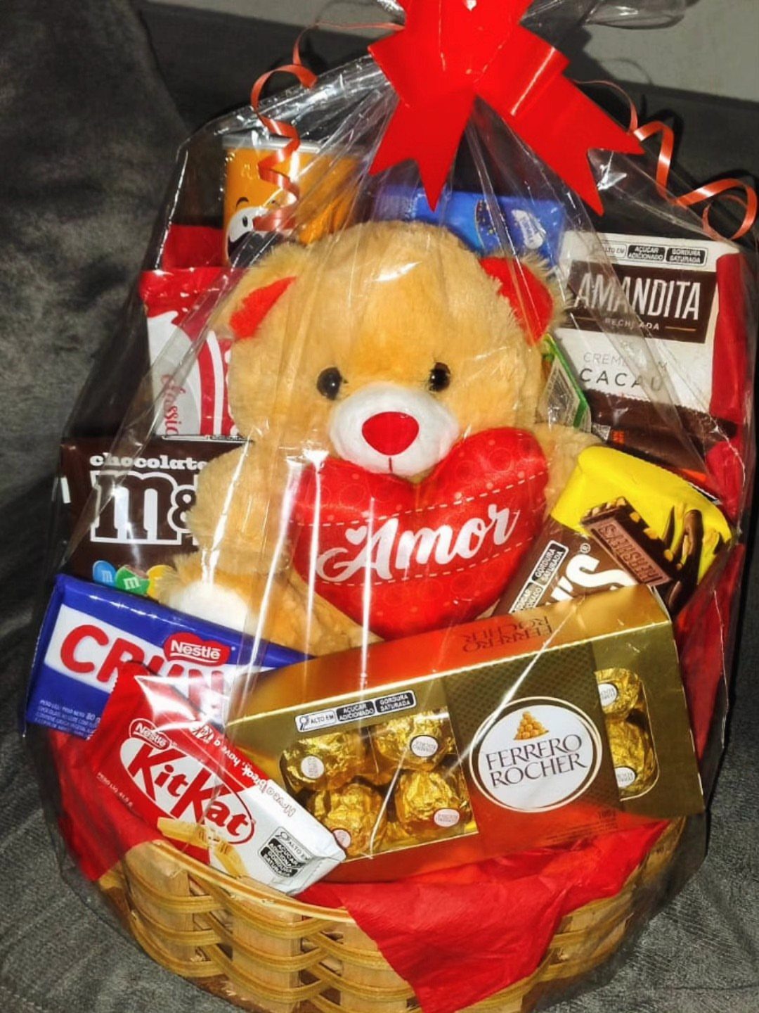 Gift basket with teddy bear and various chocolates wrapped in clear cellophane.