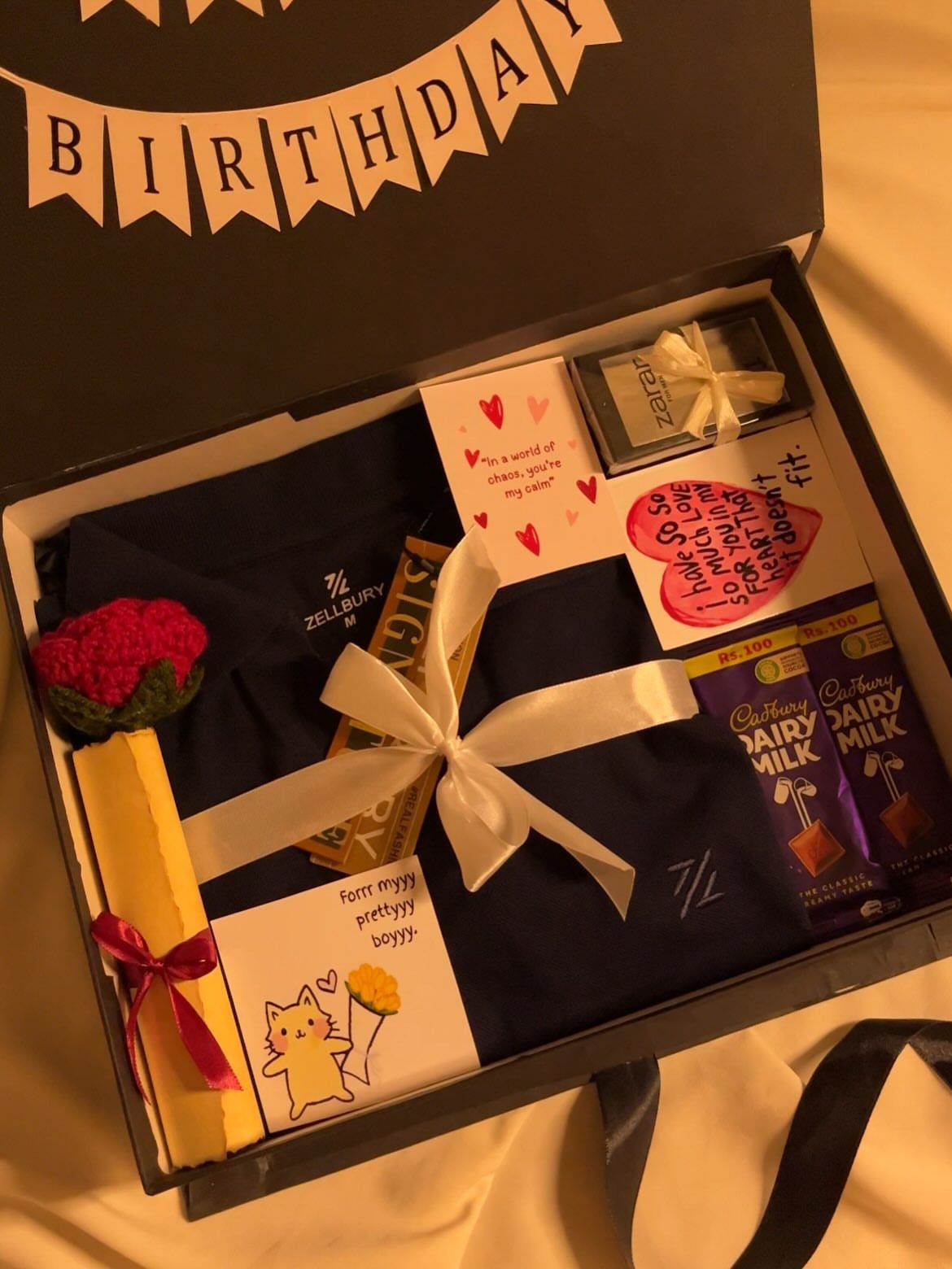 Gift box with navy shirt, chocolate bars, and handwritten notes for a boyfriend.