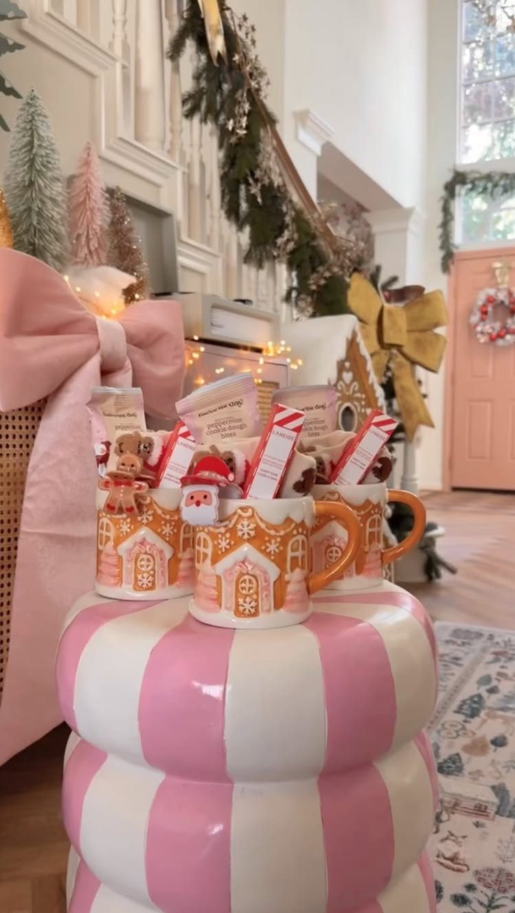 Gingerbread house mugs filled with hot chocolate mix and candy canes on a pedestal.