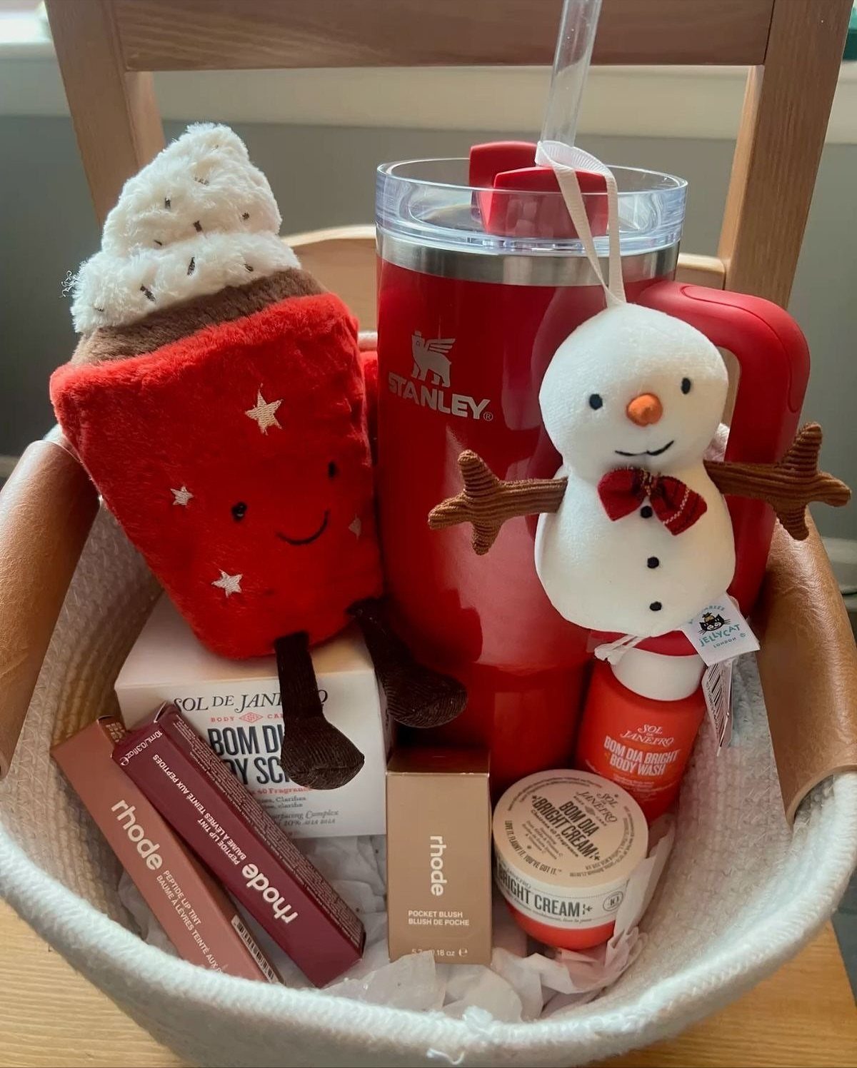 Christmas gift basket with red Stanley tumbler, plush toys, and various skincare products.