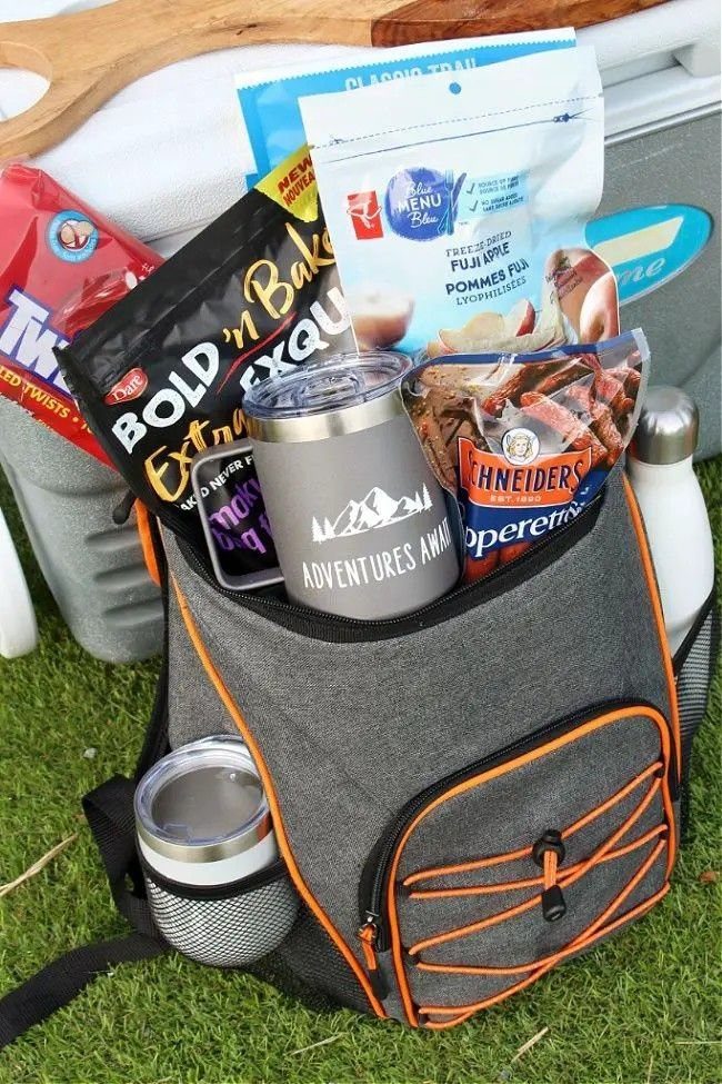 Grey gear bag filled with camping snacks and a travel mug on grass.