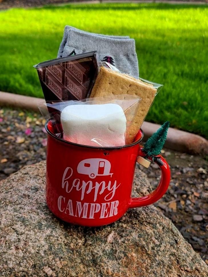 Red happy camper mug filled with s'mores ingredients and socks on a rock