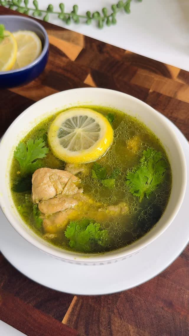 Chicken soup with lemon and parsley in a white bowl on wood.