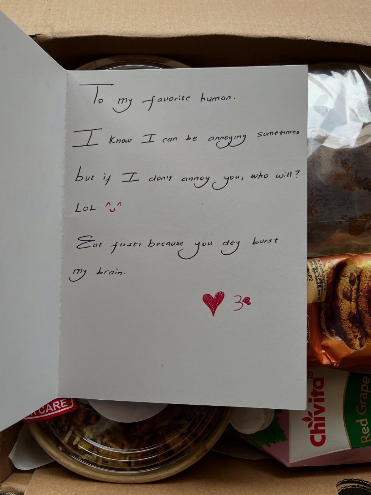 Handwritten note with a red heart inside a care package with food snacks
