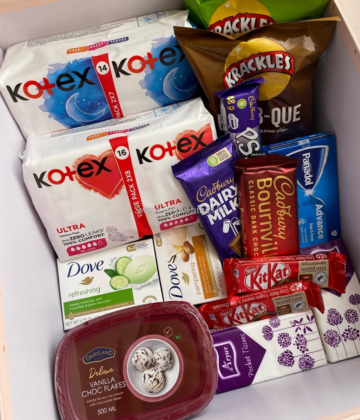 Care package box containing sanitary pads, chocolates, soap, and pain relief medication.