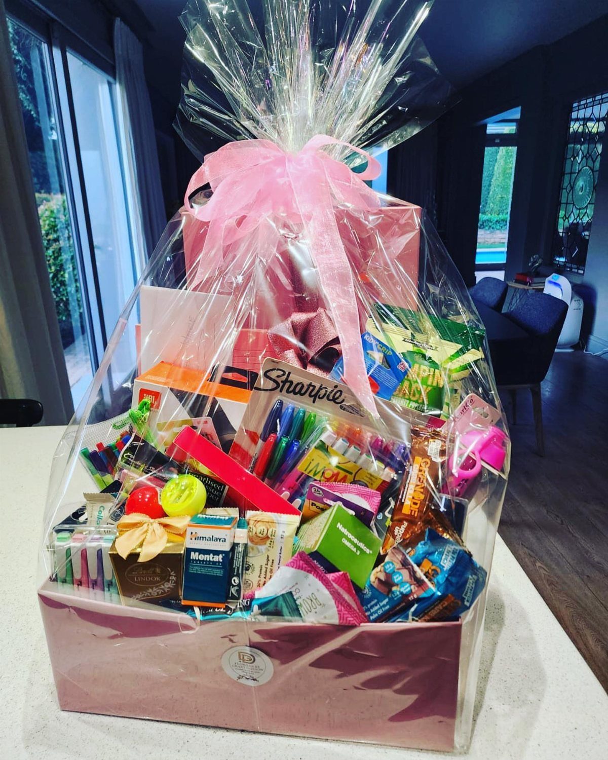 Gift basket wrapped in cellophane with a pink bow containing markers and snacks.