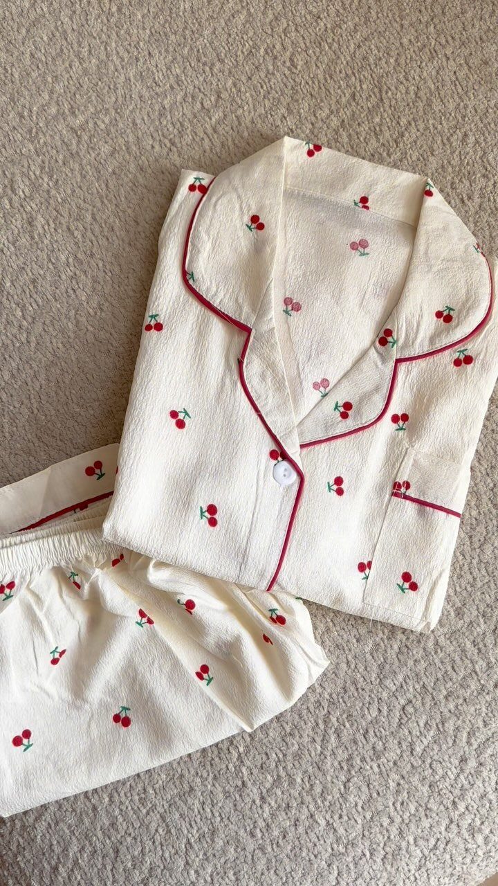 Cream-colored pajamas with red cherry patterns and red piping on beige fabric.