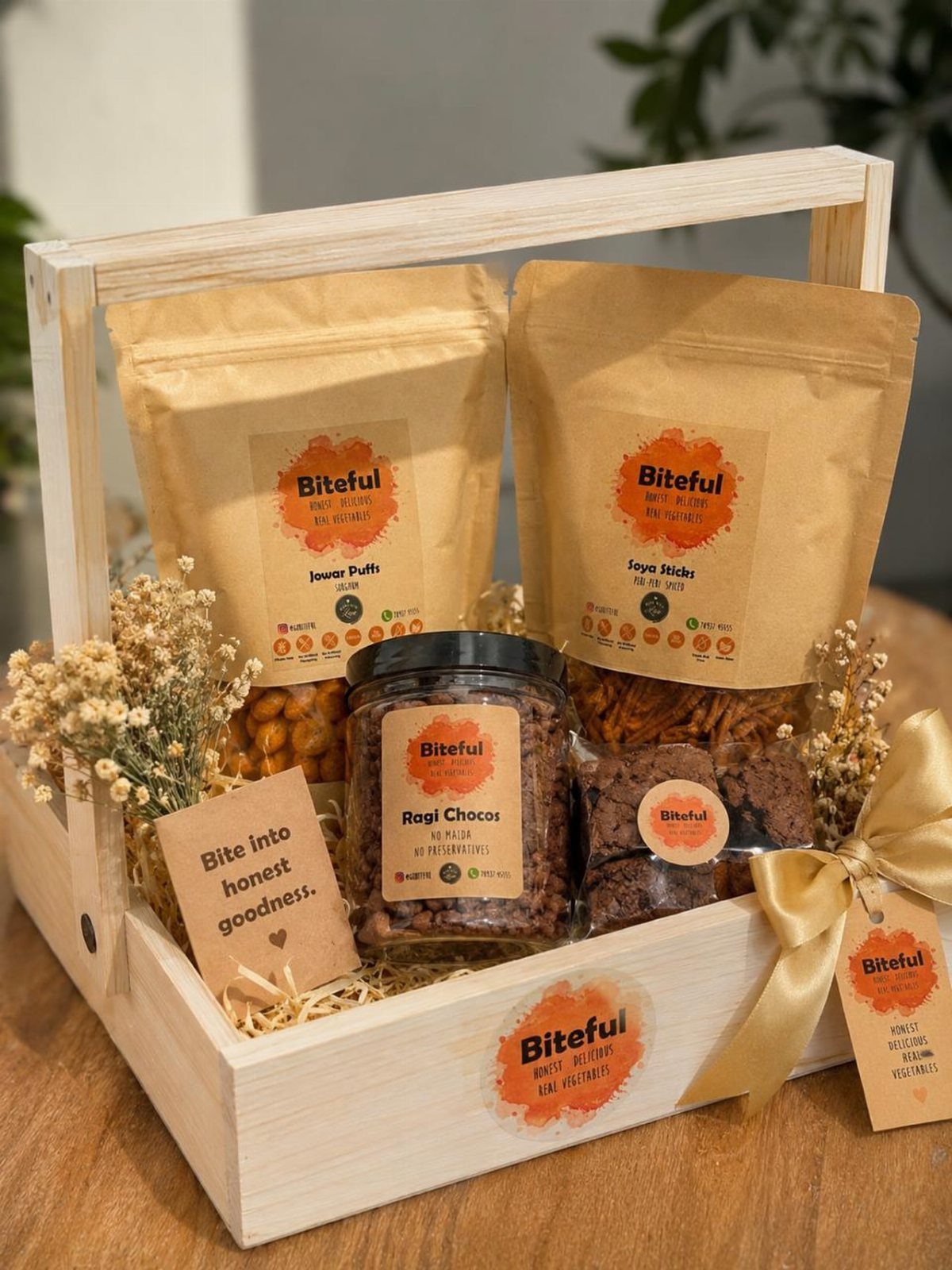 Wooden gift crate filled with Biteful branded healthy snacks and dried flowers.