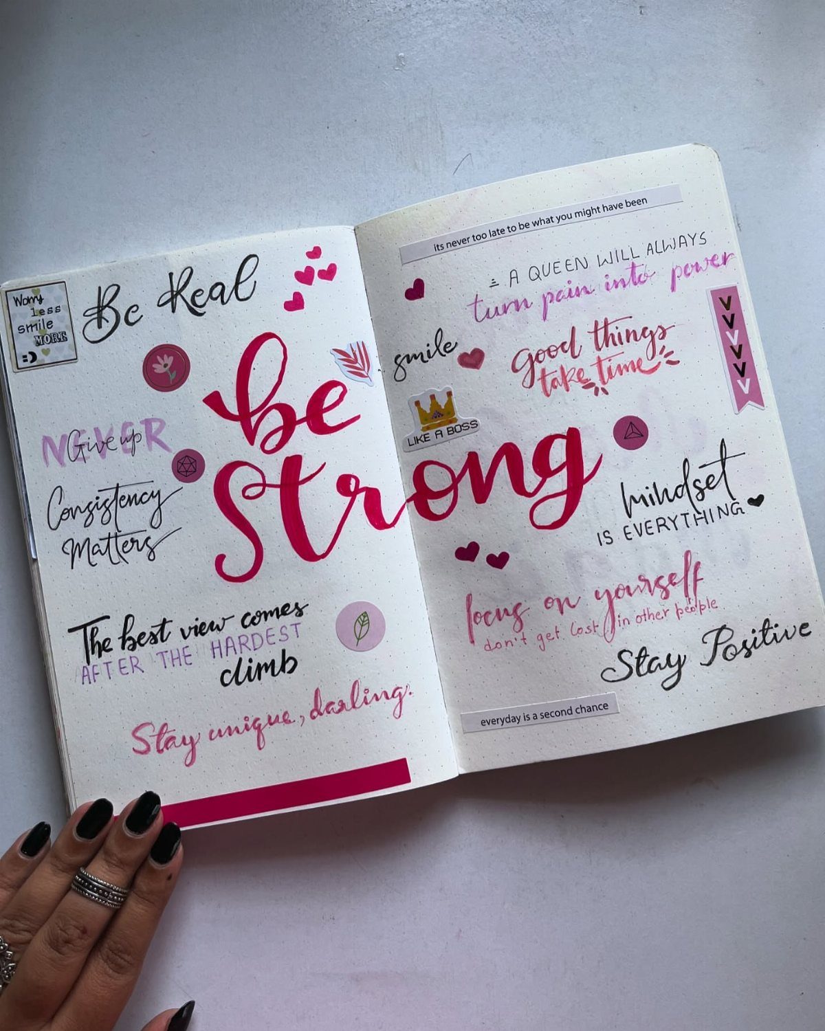 Open journal with handwritten inspirational quotes in pink and black ink on white pages.
