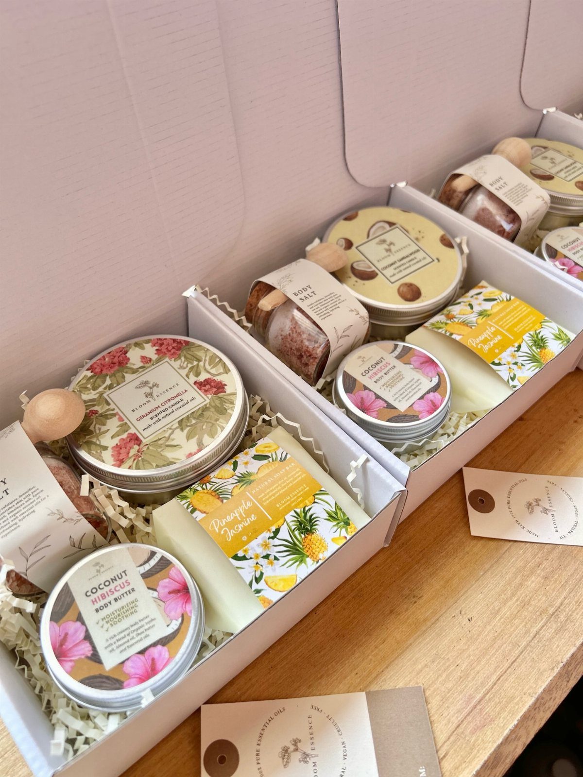 Three gift boxes filled with body butter, soaps, and skincare products on wood.