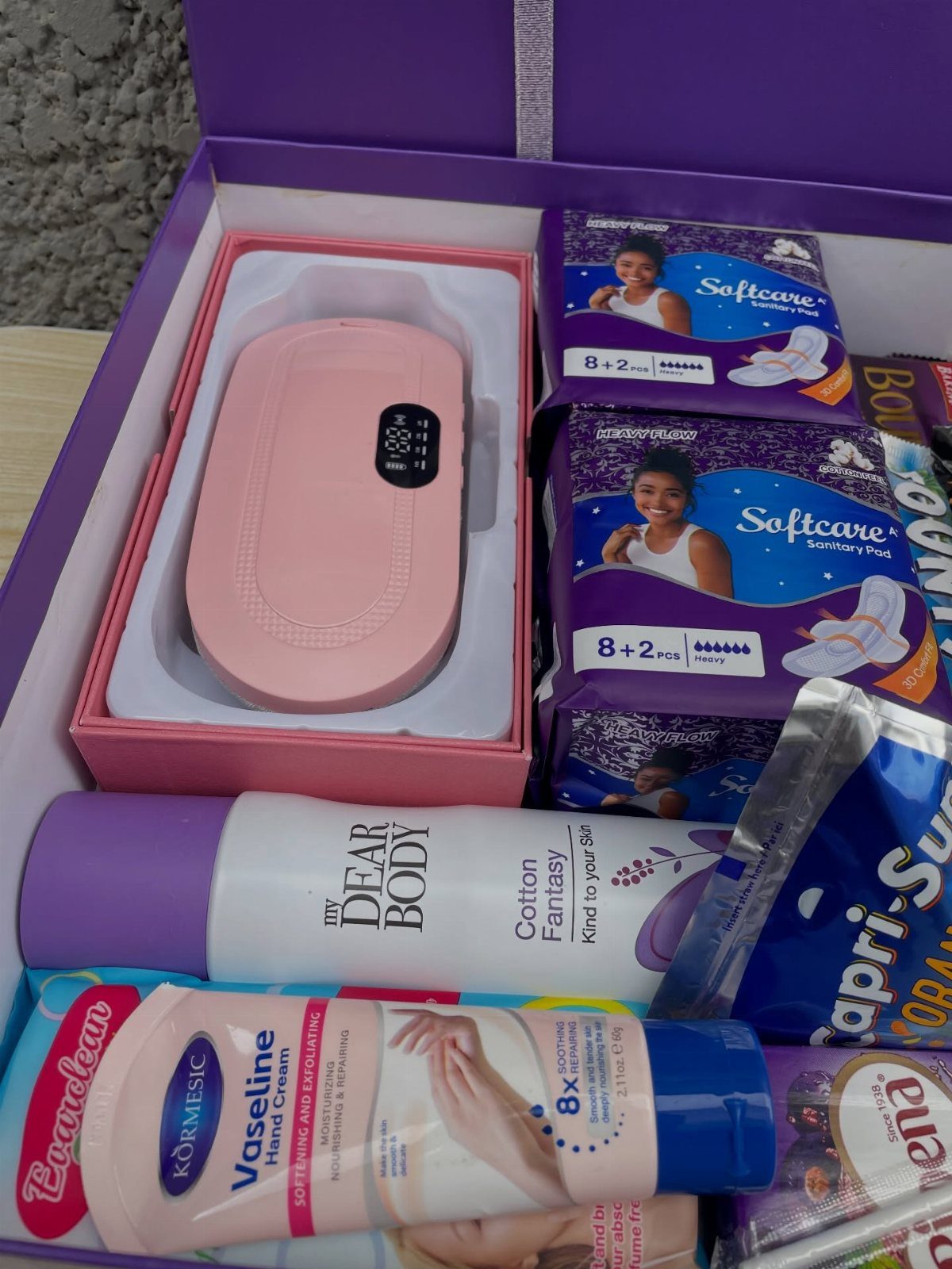 Purple gift box containing a pink electronic device, sanitary pads, and skincare lotions.
