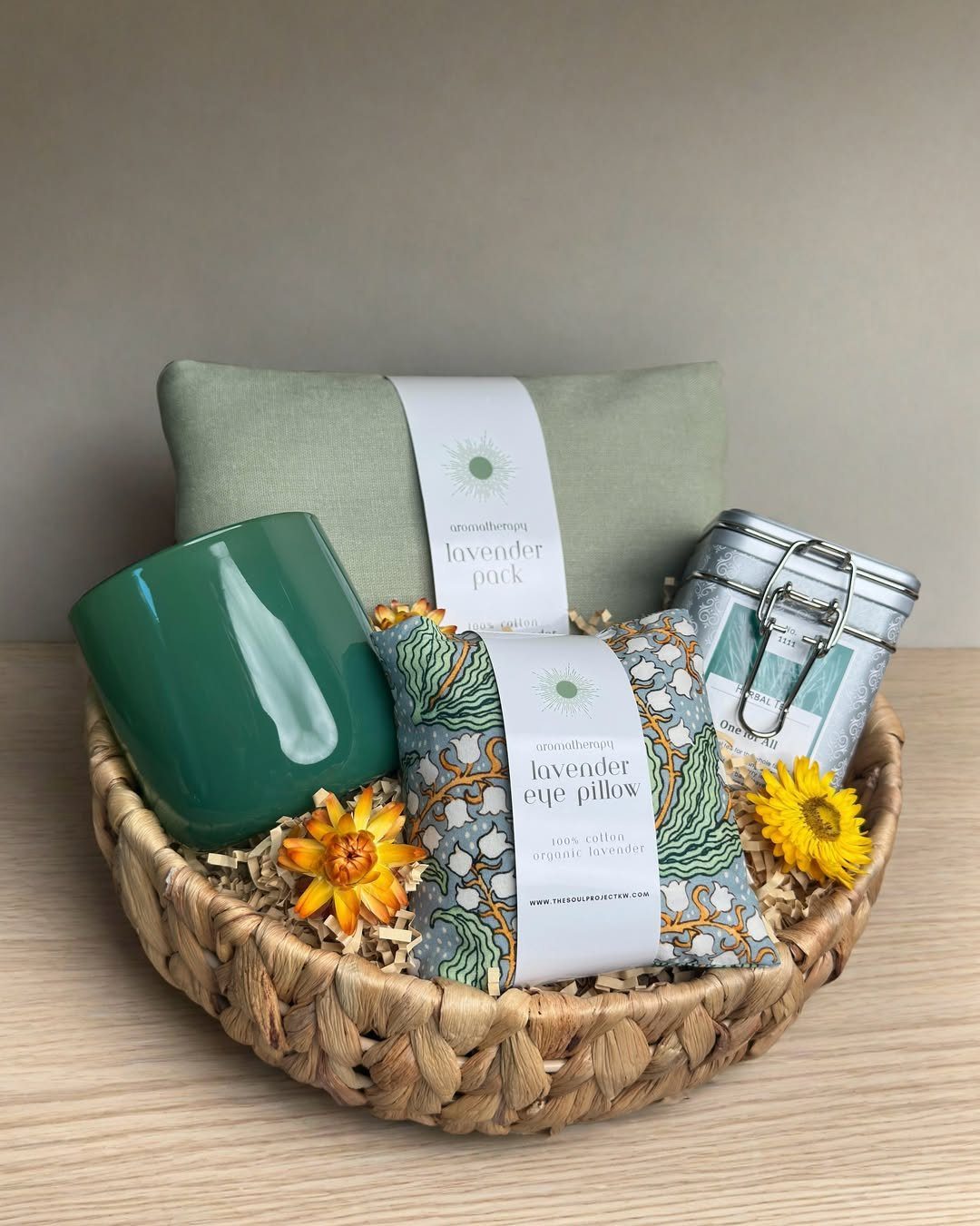Woven gift basket with green mug, lavender packs, and yellow flowers on wood.