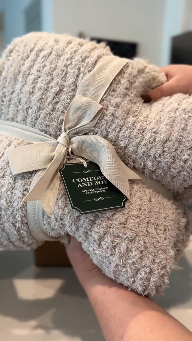 Folded beige fluffy blanket tied with a cream ribbon and a gift tag.
