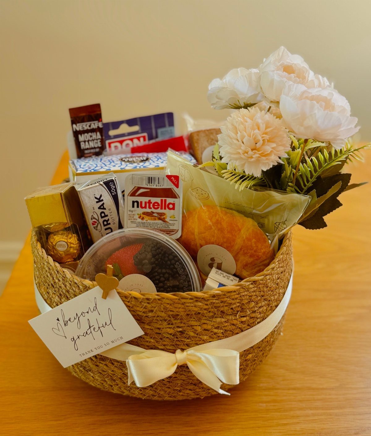 Woven gift basket filled with breakfast foods, coffee, and white flowers.