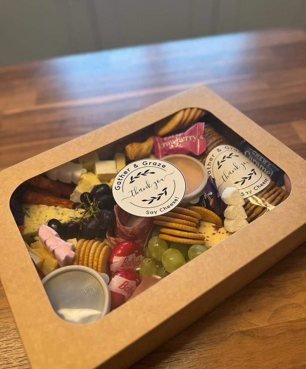 Charcuterie gift box with assorted cheeses, grapes, crackers, and meats on wooden table