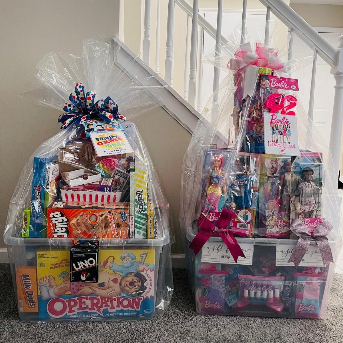 Two gift baskets, one filled with board games and snacks, one with Barbie dolls.