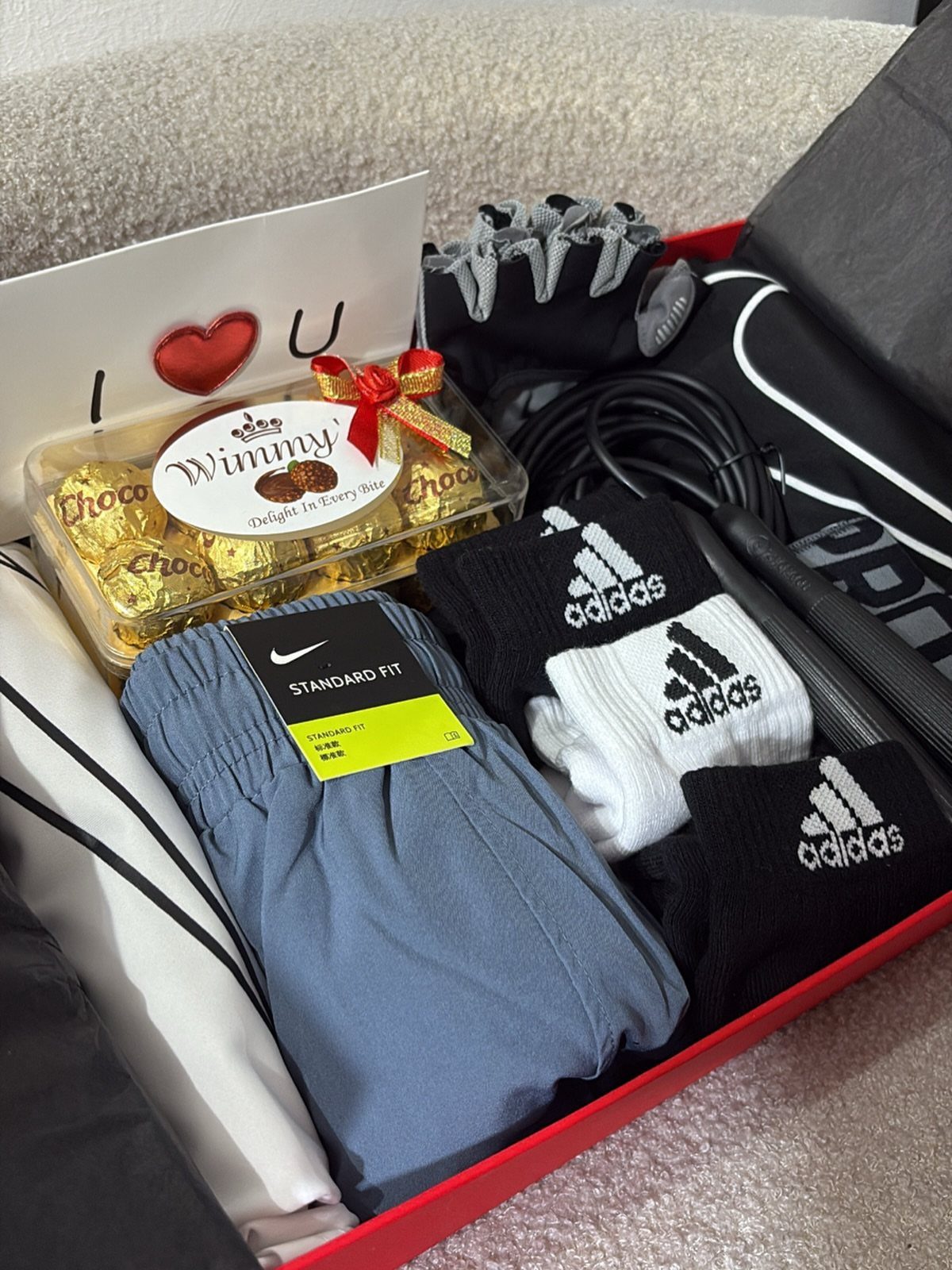 Fitness gift basket with blue athletic pants, Adidas socks, jump rope, and chocolates.