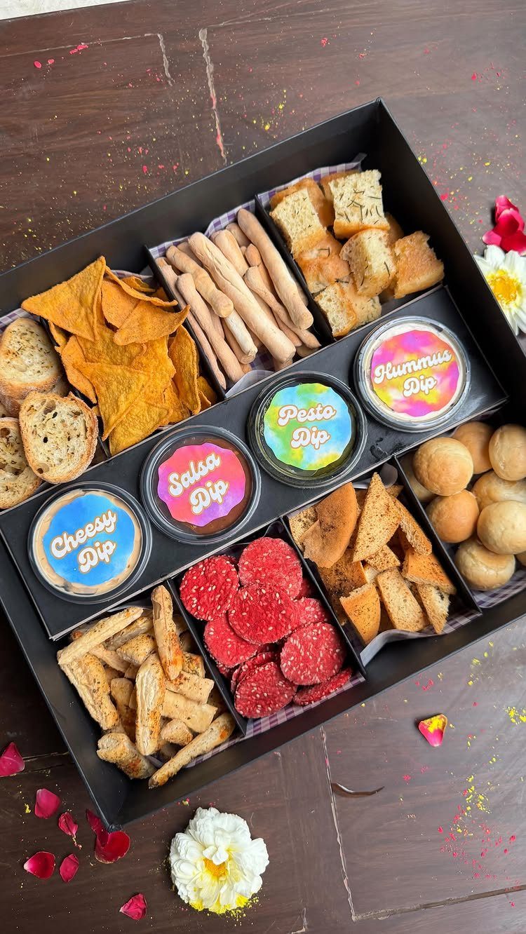 Snack gift box with chips, bread, salami, and various dips on wooden table