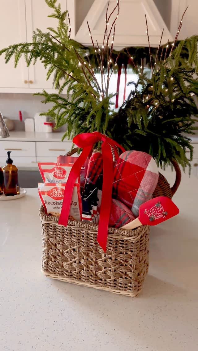 Woven gift basket with red ribbon, plaid fabric, and treats on white counter