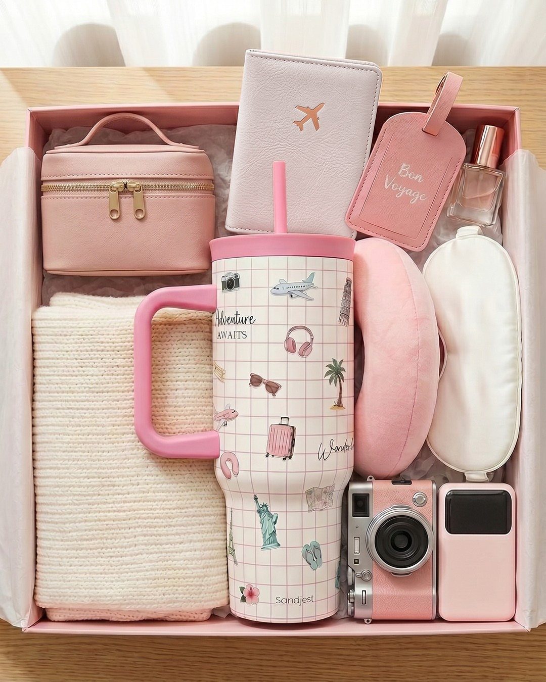 Travel essentials gift basket with pink accessories, tumbler, and neck pillow in a box.