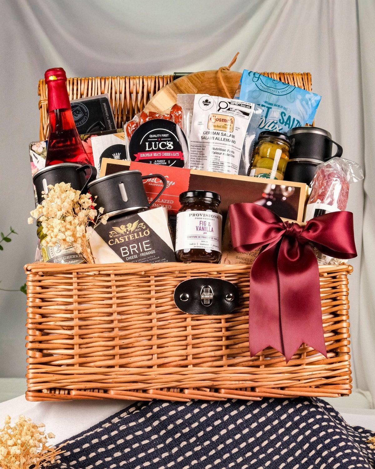 Wicker gift basket with wine, brie cheese, and gourmet snacks tied with burgundy bow