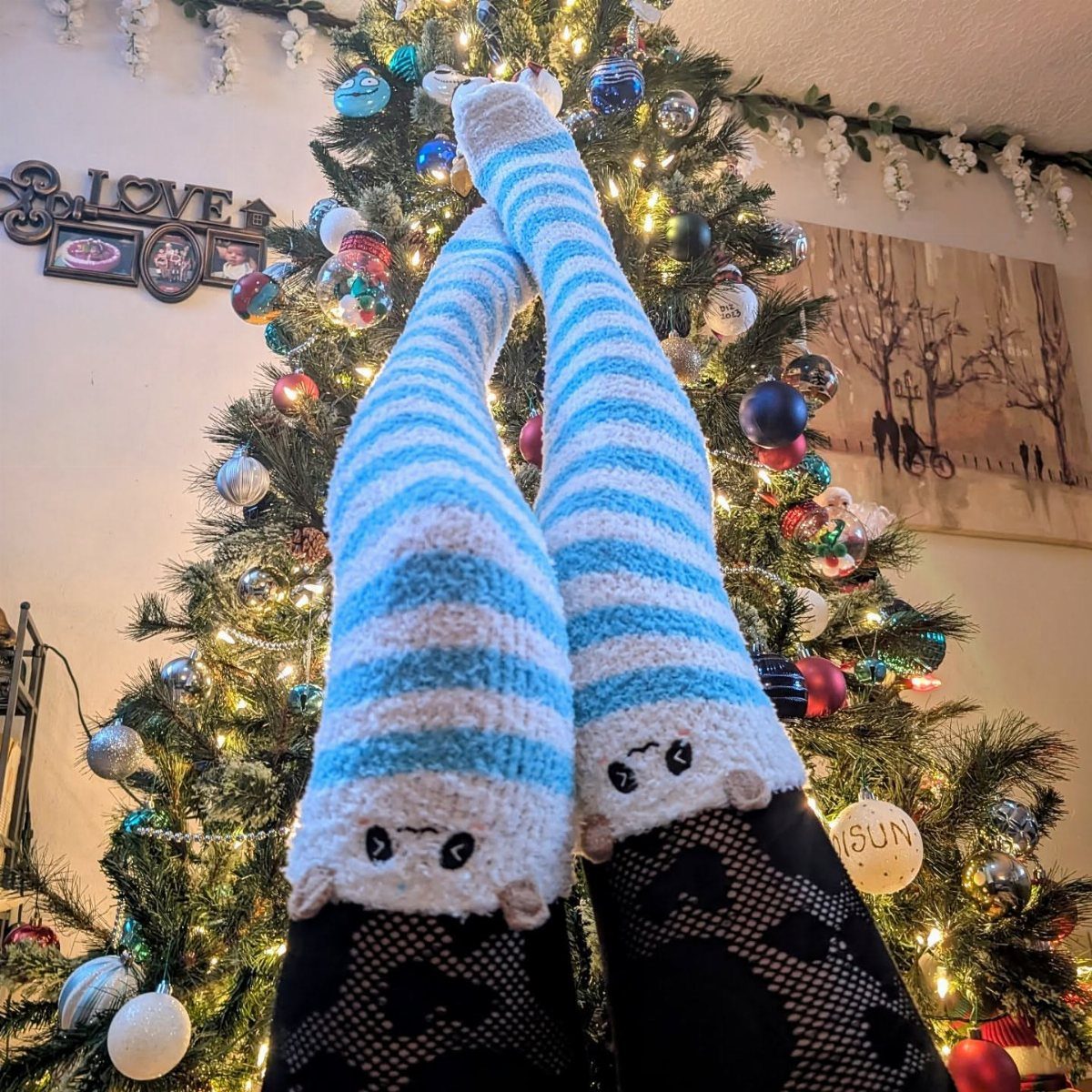 Blue and white striped fuzzy socks with faces in front of Christmas tree