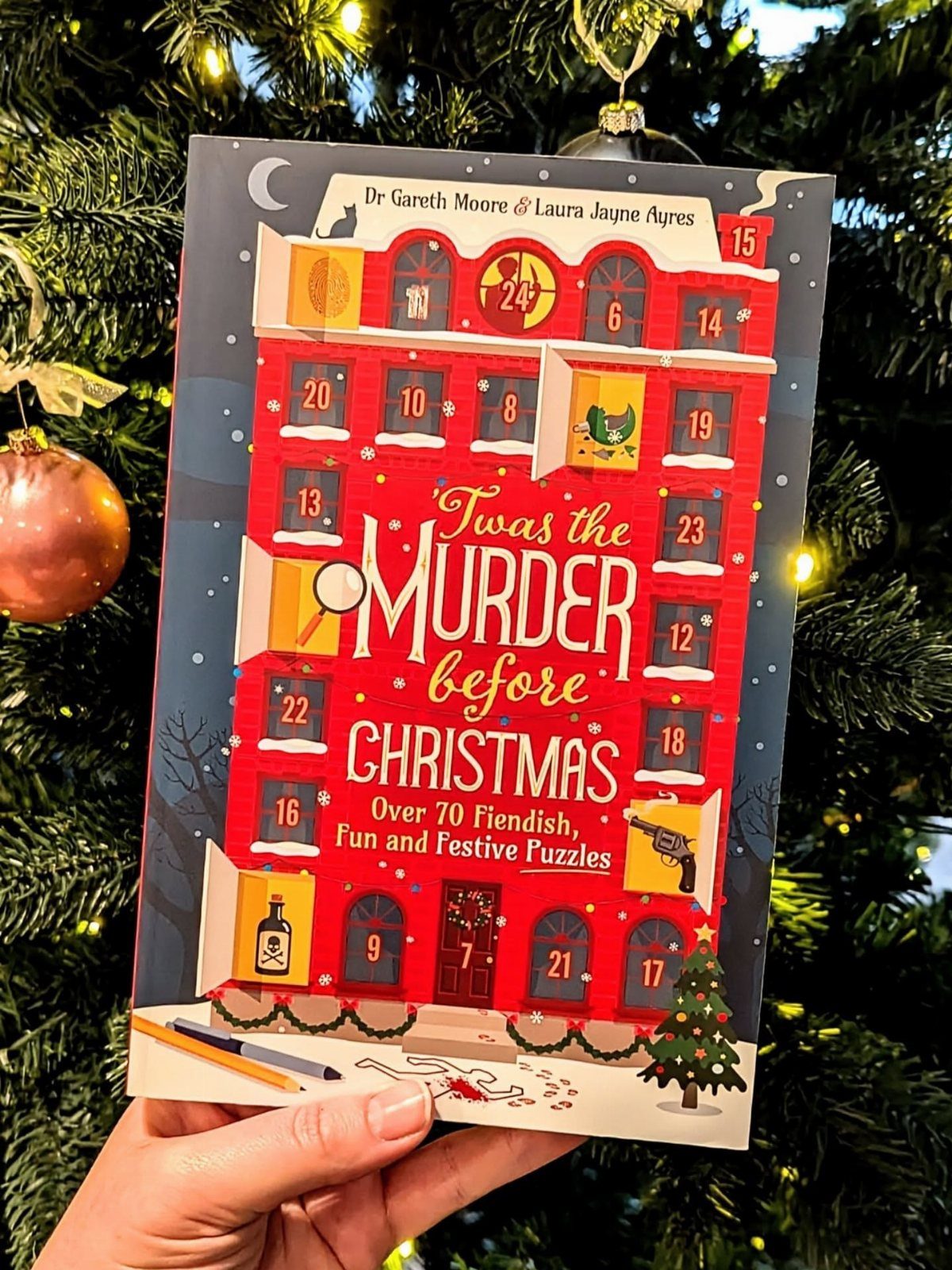 Christmas puzzle book held in front of a lit holiday tree with ornaments.