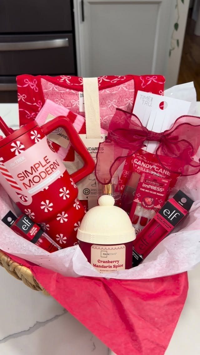 Wicker basket filled with red Christmas gifts, a tumbler, and a scented candle.