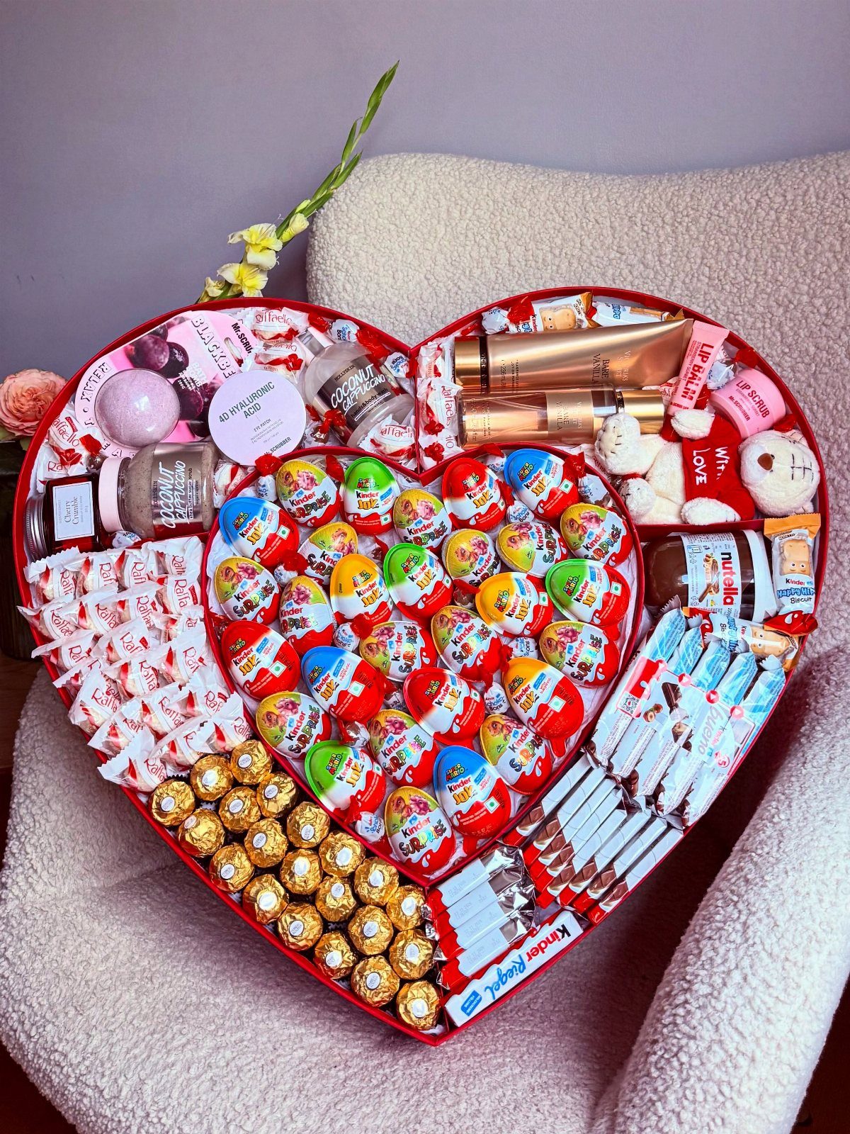 Heart-shaped red gift box filled with chocolates, Kinder eggs, and beauty products.