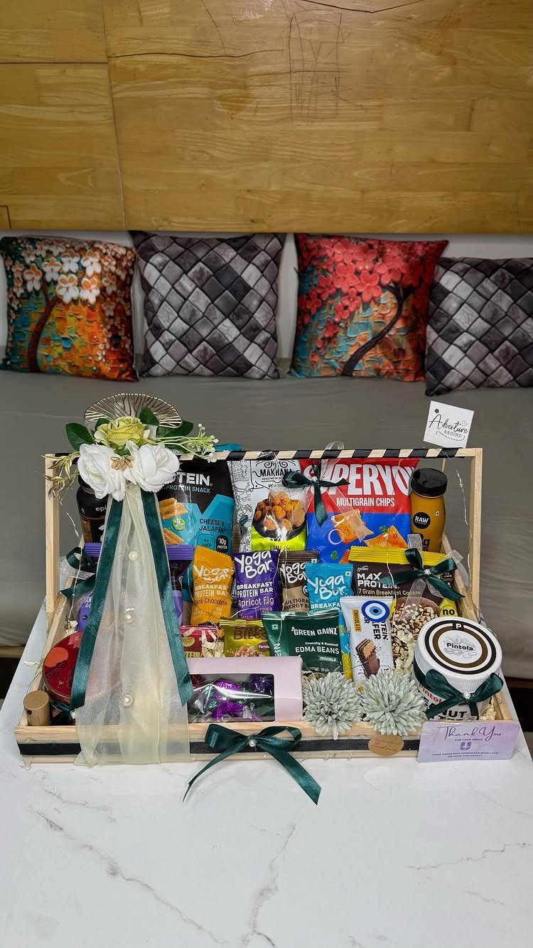 Wooden gift crate filled with healthy snacks, decorated with white flowers and green ribbons.