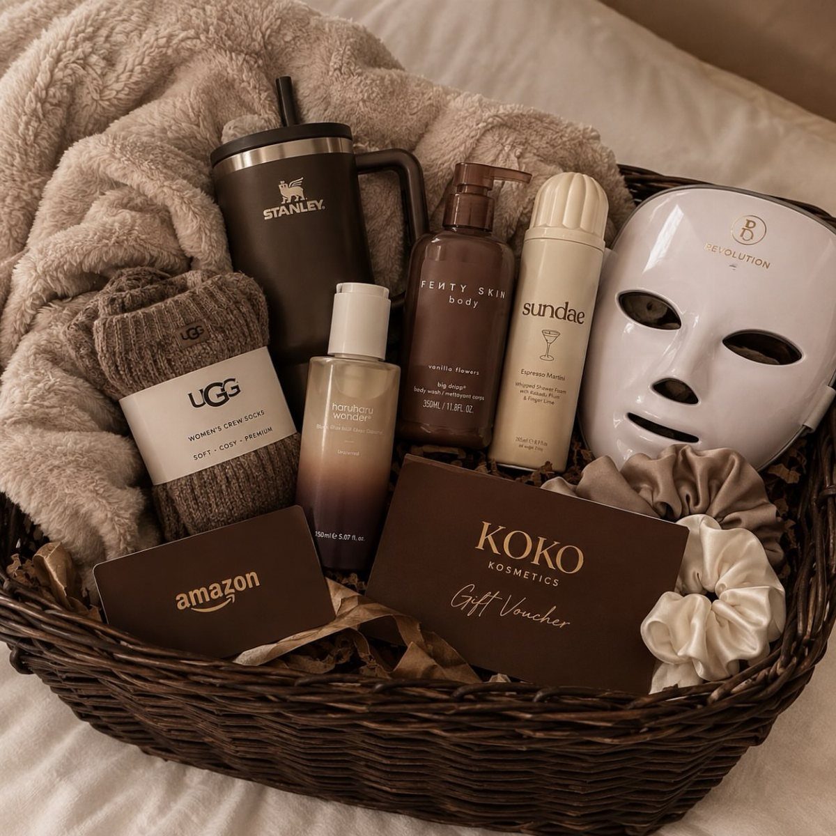 Wicker gift basket with LED face mask, skincare products, and cozy accessories.